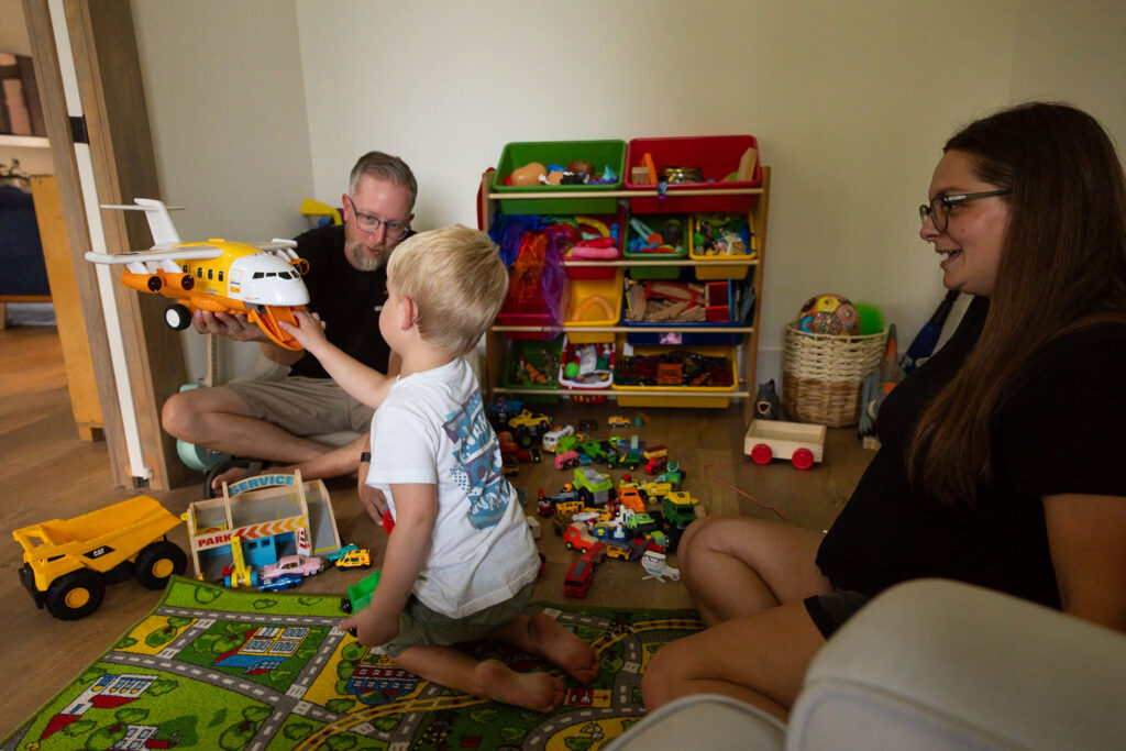 Mom, dad, and young son playing together among toys in the living room.