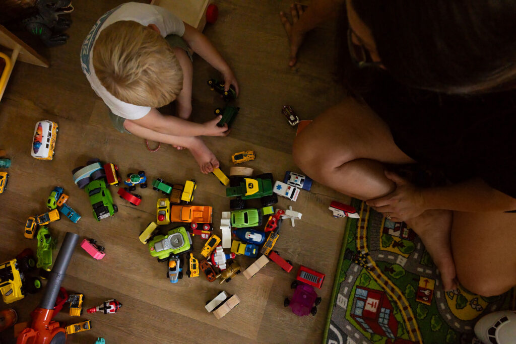 Overhead view of mom and young son playing with toy cars on the floor.