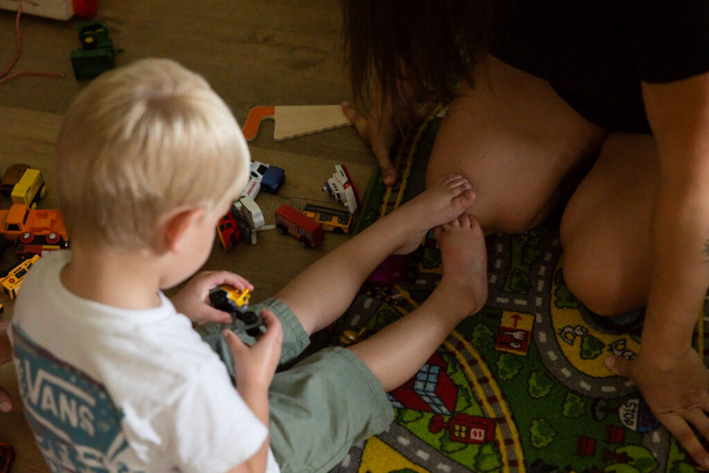Close-up of mom and young son playing together with toys on the floor while the boy rests his feet against his mom's knee.
