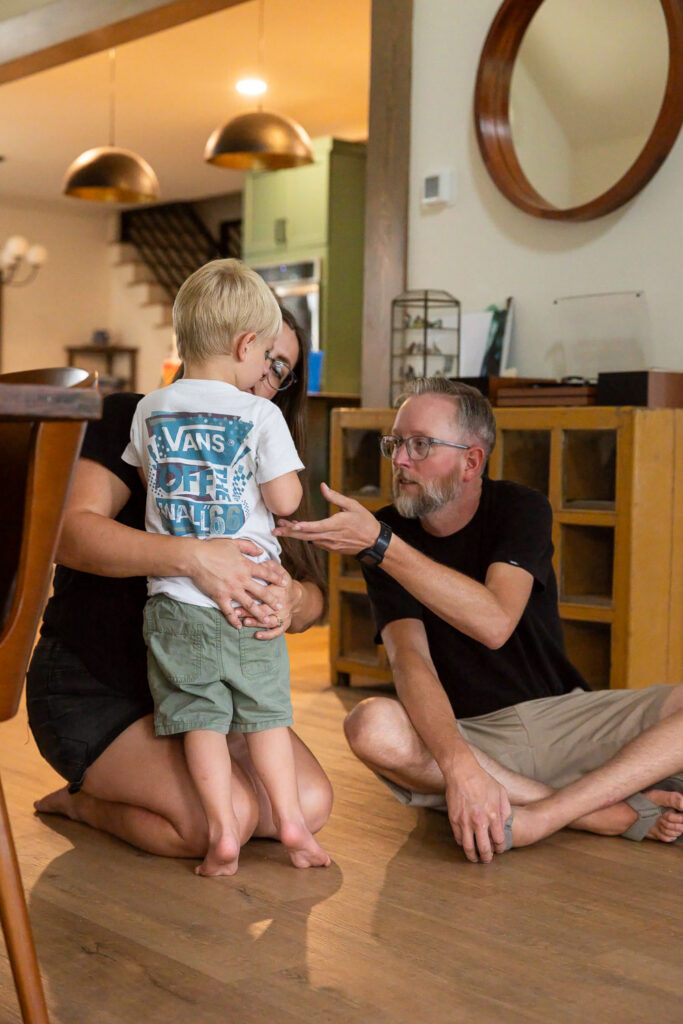 A tender moment when mom hugs her toddler son in close and dad reaches a hand toward him for extra comfort.