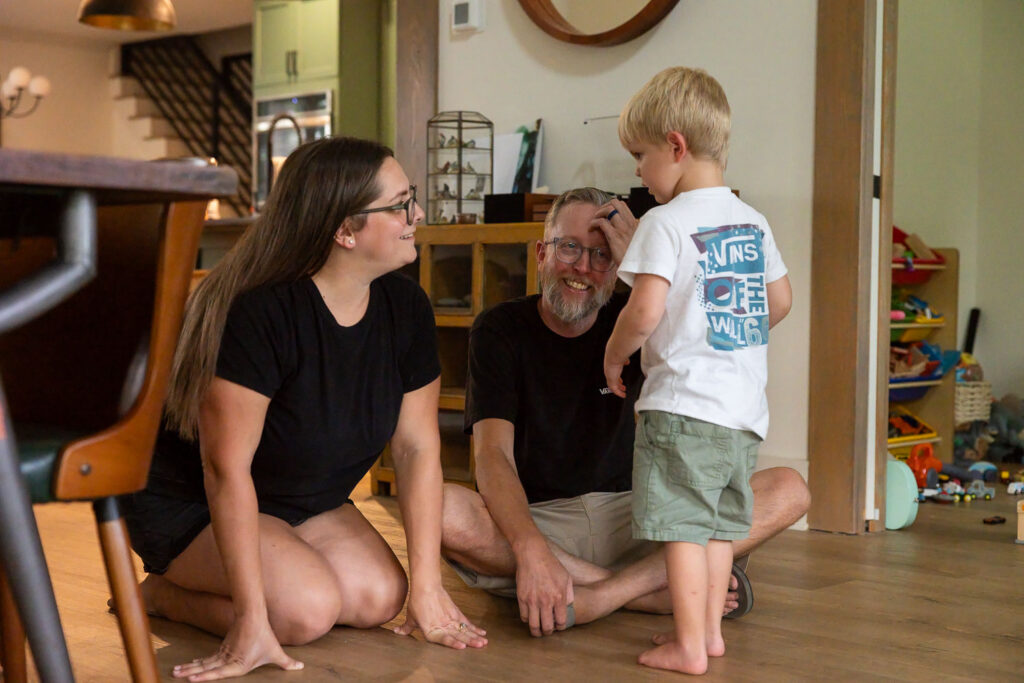 Mom, dad, and young son gathered on the floor together with smiles on their faces.